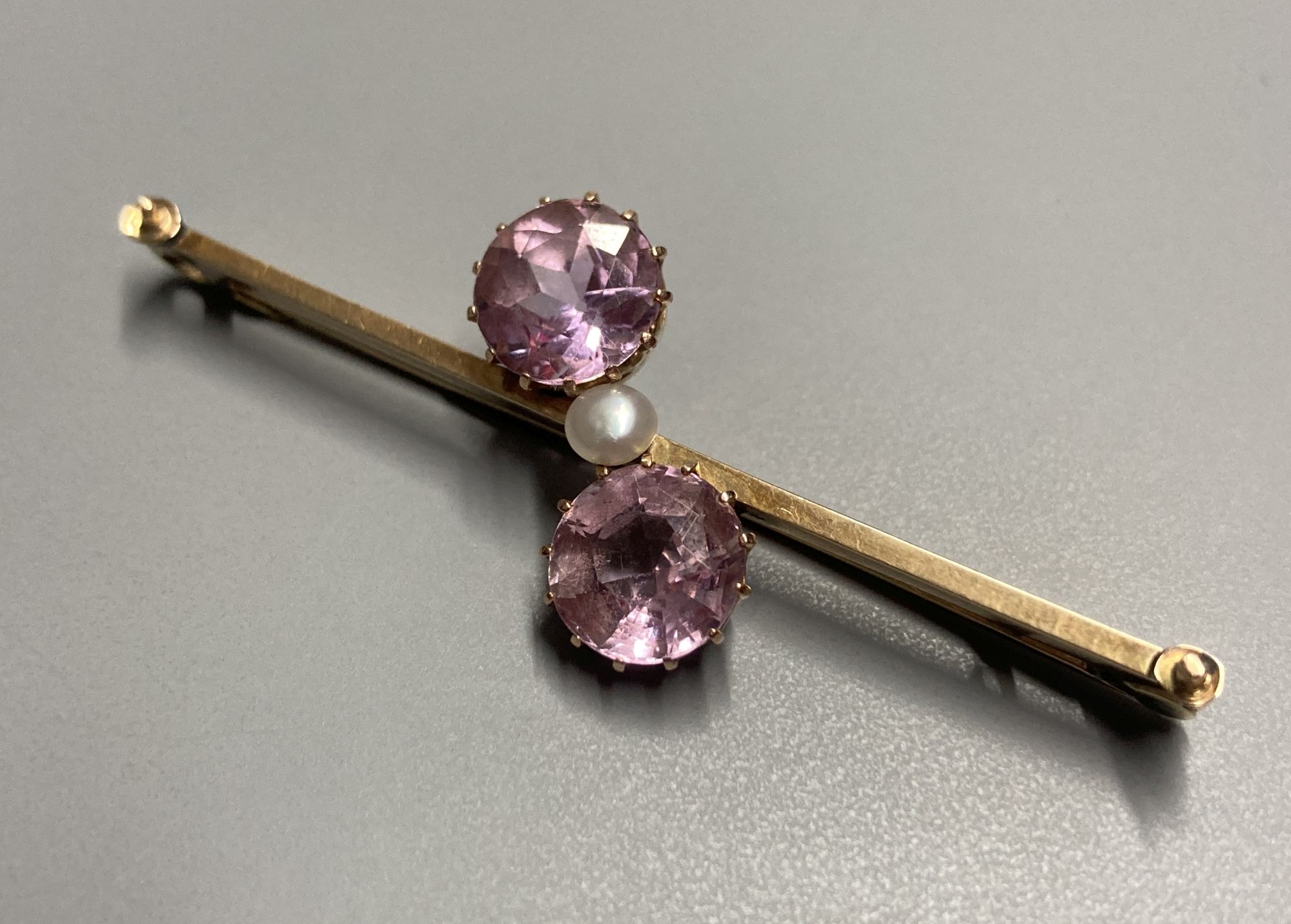 An early 20th century 15ct and three stone pink topaz and seed pearl set crossover bar brooch, 50mm, gross 4.4 grams.